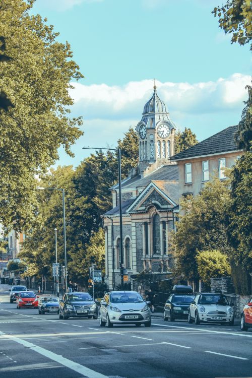Free Street view in Bristol featuring a historic clock tower, lined with cars and lush trees. Stock Photo