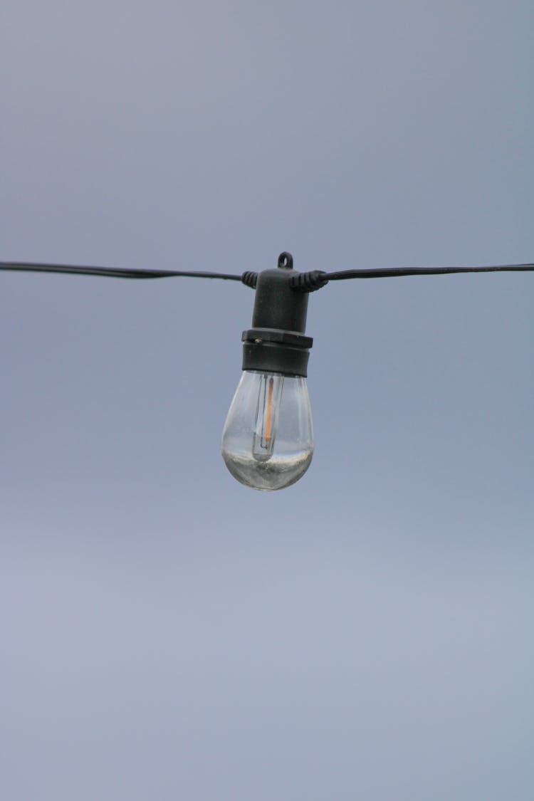 Lightbulb Hanging On Wires On Sky Background