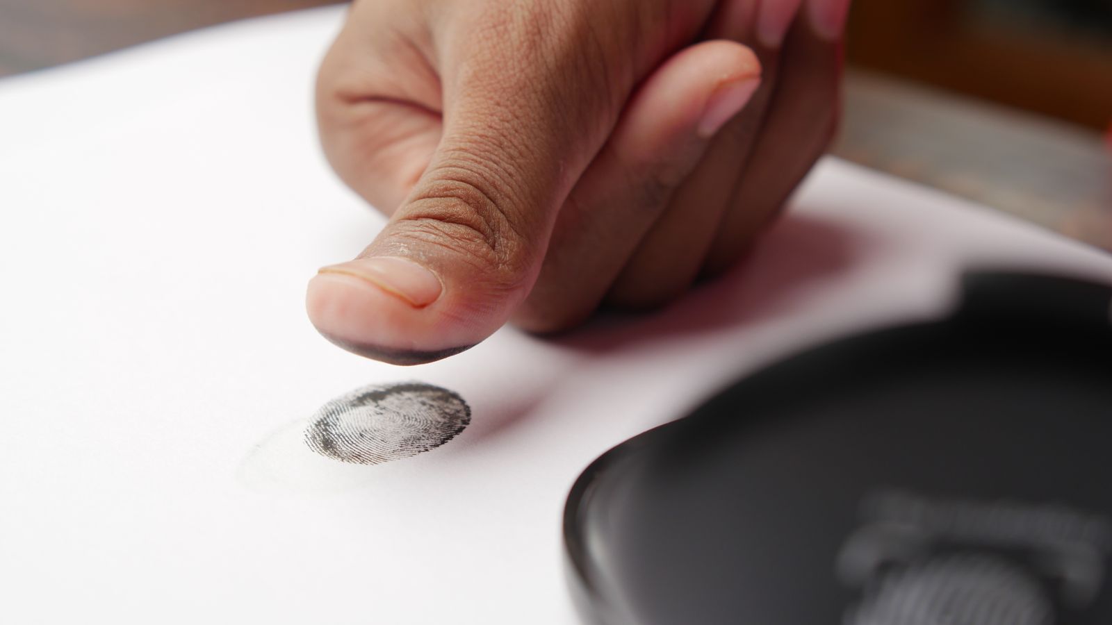 Detailed shot of a thumb creating a fingerprint on white paper, ideal for security themes.