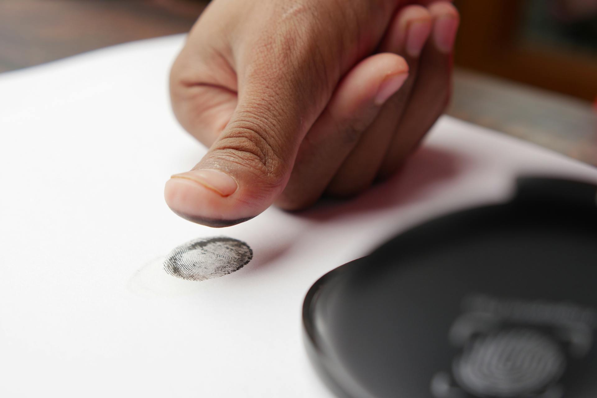 Detailed shot of a thumb creating a fingerprint on white paper, ideal for security themes.