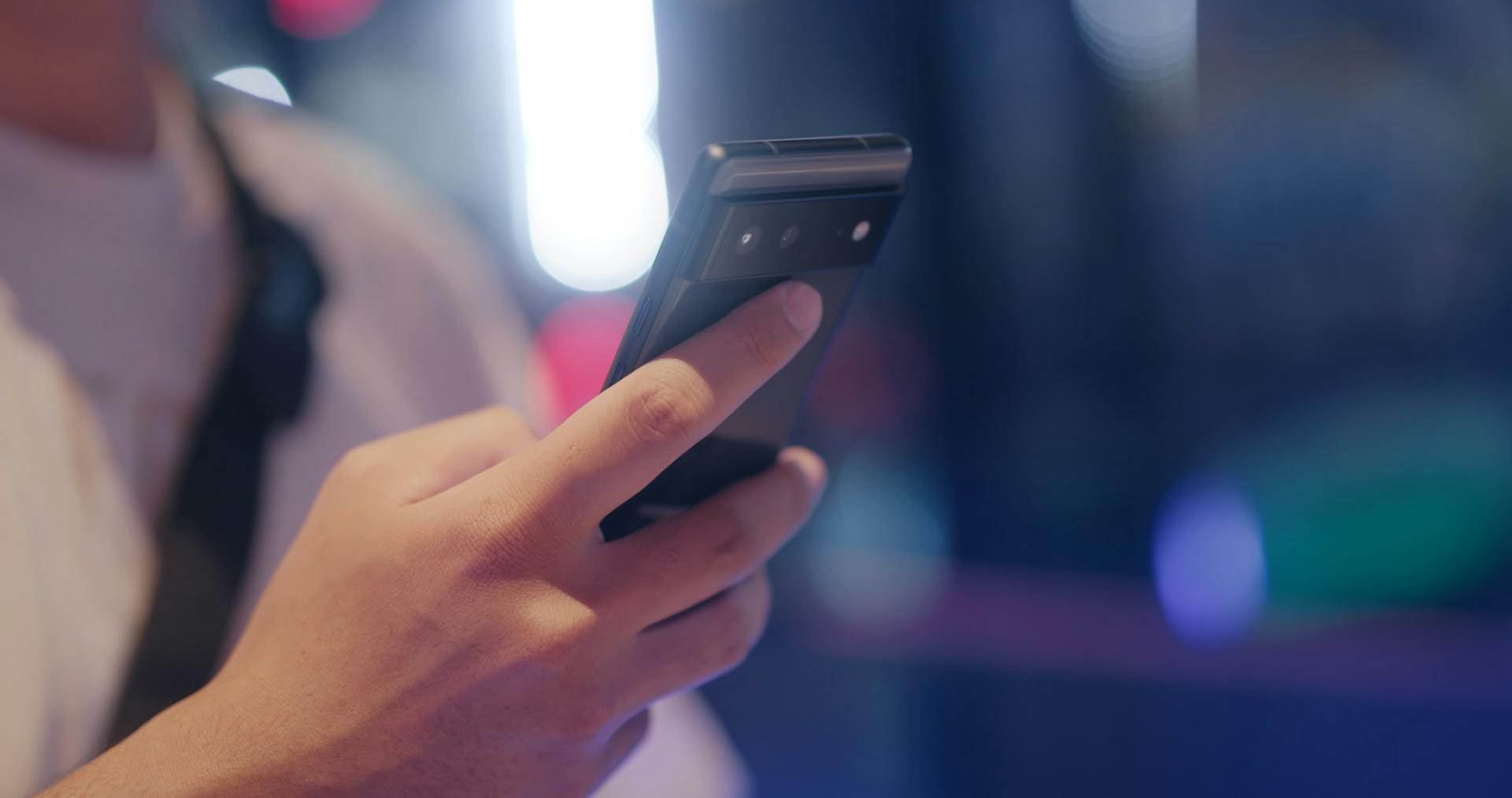 A close-up view of a person holding and using a smartphone outdoors at night.