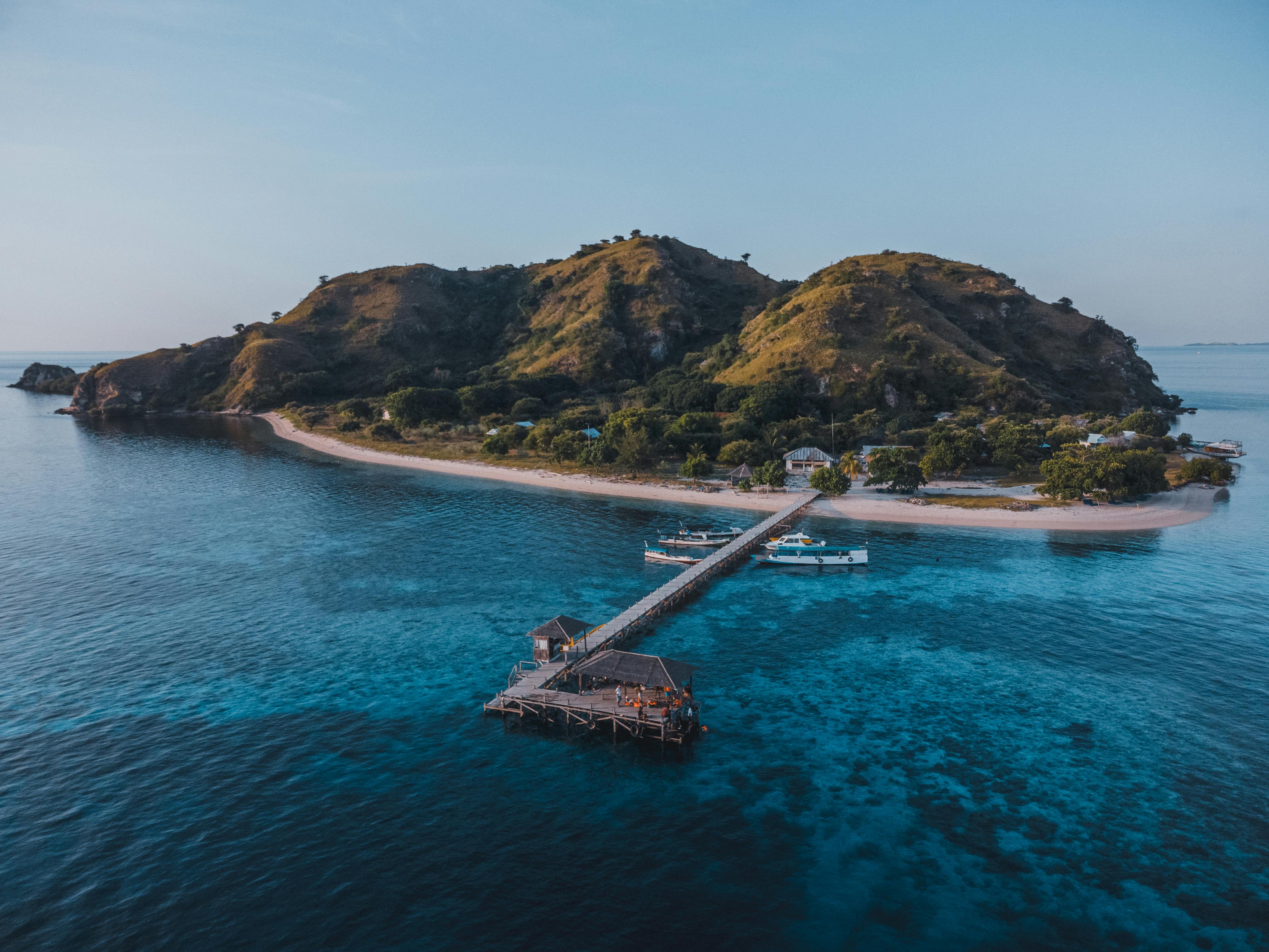 aerial view of Kanawa Island near Labuan Bajo showing white sandy shoreline, shallow turquoise waters, and coral reefs surrounding the island.