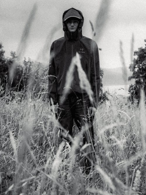 Grayscale Photo of Man in Black Jacket Standing on Grass Field