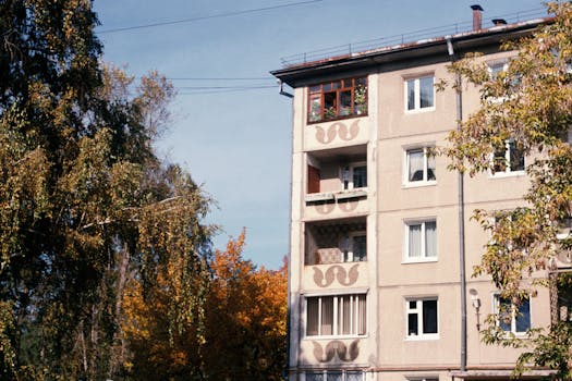 A city apartment building surrounded by autumn trees under a clear blue sky.