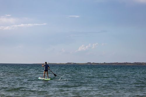Free A man paddleboarding on a calm ocean under a clear blue sky, showcasing outdoor leisure and recreation. Stock Photo