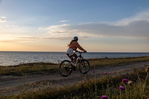 Woman in a Long Sleeve Shirt Riding a Bike Near the Sea