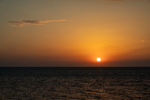 A breathtaking view of the sun setting over the ocean, creating an orange sky.