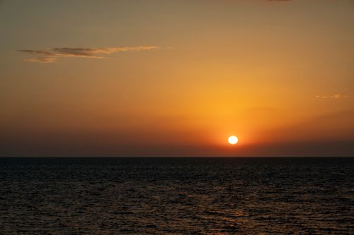 Free A breathtaking view of the sun setting over the ocean, creating an orange sky. Stock Photo