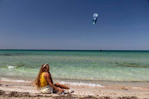 Free A woman enjoys a sunny day on the beach while a kite surfer rides in the distance. Stock Photo