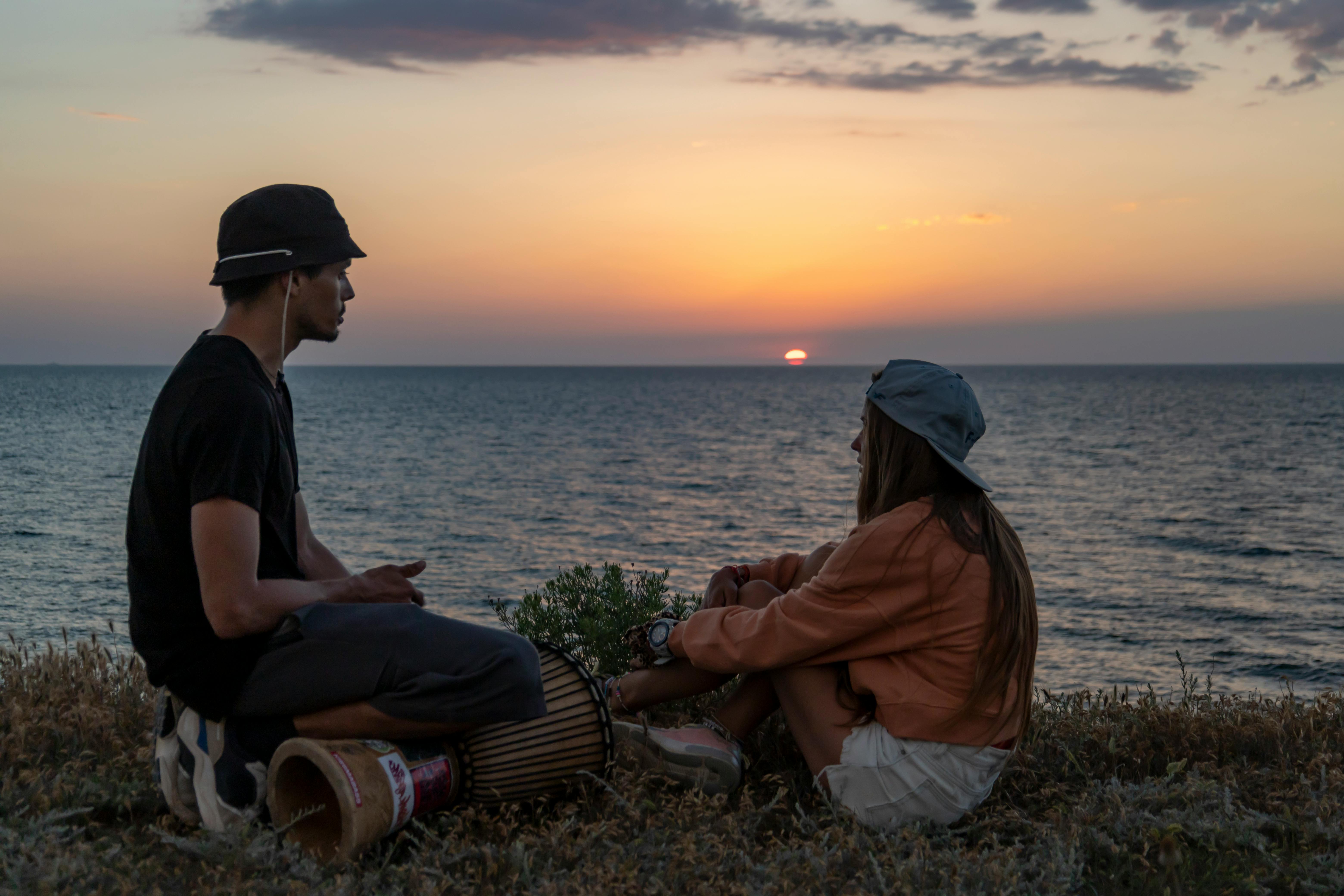 man with a drum sitting near the sea during sunset