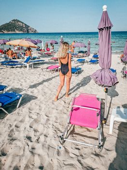 A woman in swimwear enjoys a sunny day on a lively beach with colorful umbrellas and loungers.
