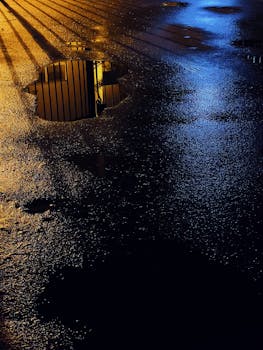 Dramatic night scene with reflections in puddles on a wet asphalt road. Captures urban street mood.