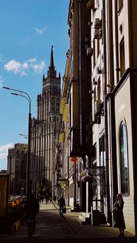 Sunlit city street view with a towering cathedral and blue sky in the background.