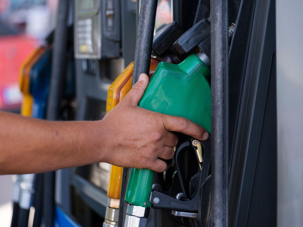 Close-up of a hand holding a green fuel nozzle at a gas pump station outdoors