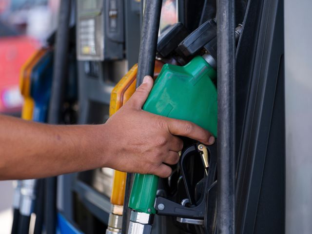 Hand holding a green fuel pump nozzle on a service-station dispenser.