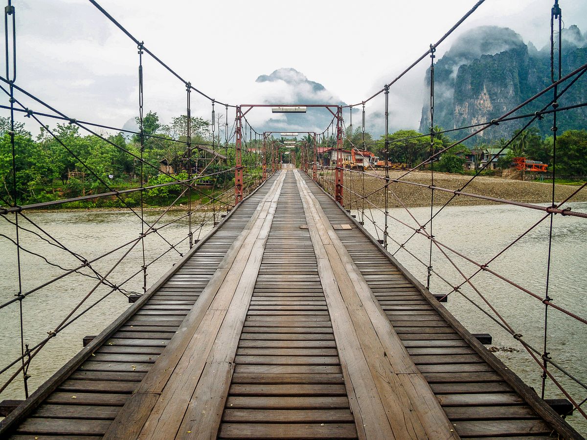 Wooden suspension bridge over the river below misty karst peaks, Vang Vieng