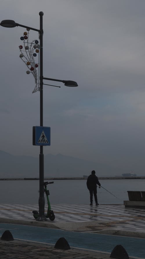 A Person om Black Jacket Standing on the Riverside Holding a Fishing Rod