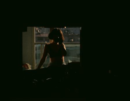 Moody silhouette of a woman sitting by a window with urban backdrop.