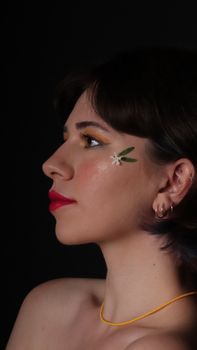Close-up side profile of a woman with artistic floral makeup against a dark background.