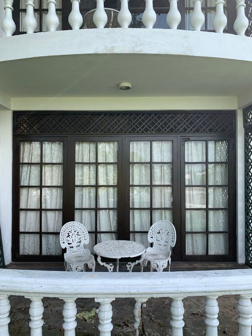 Free An inviting outdoor balcony with vintage white chairs and table against classic glass doors. Stock Photo