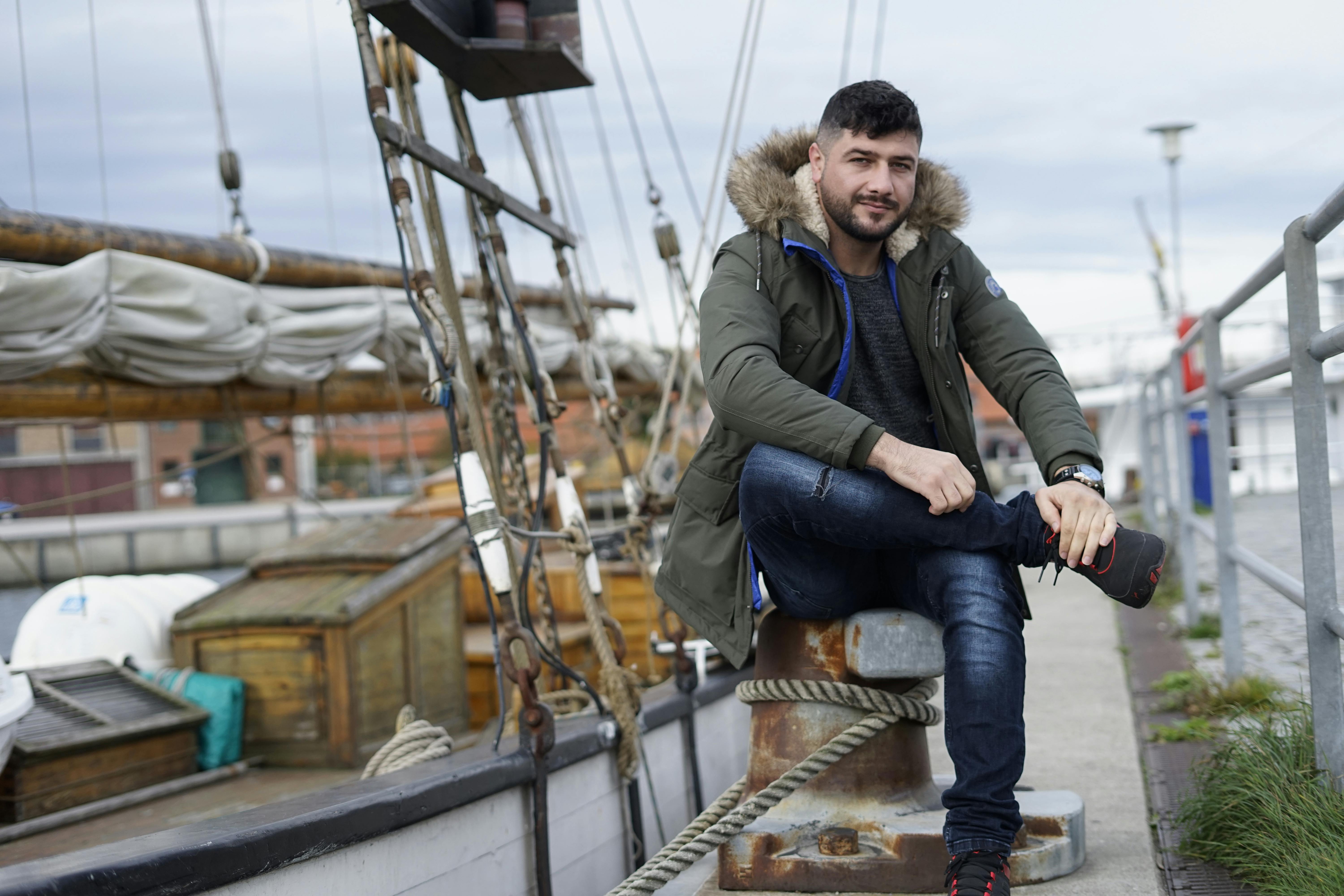 A man sitting on a pier by a sailing boat in winter at Bocholt, Germany.