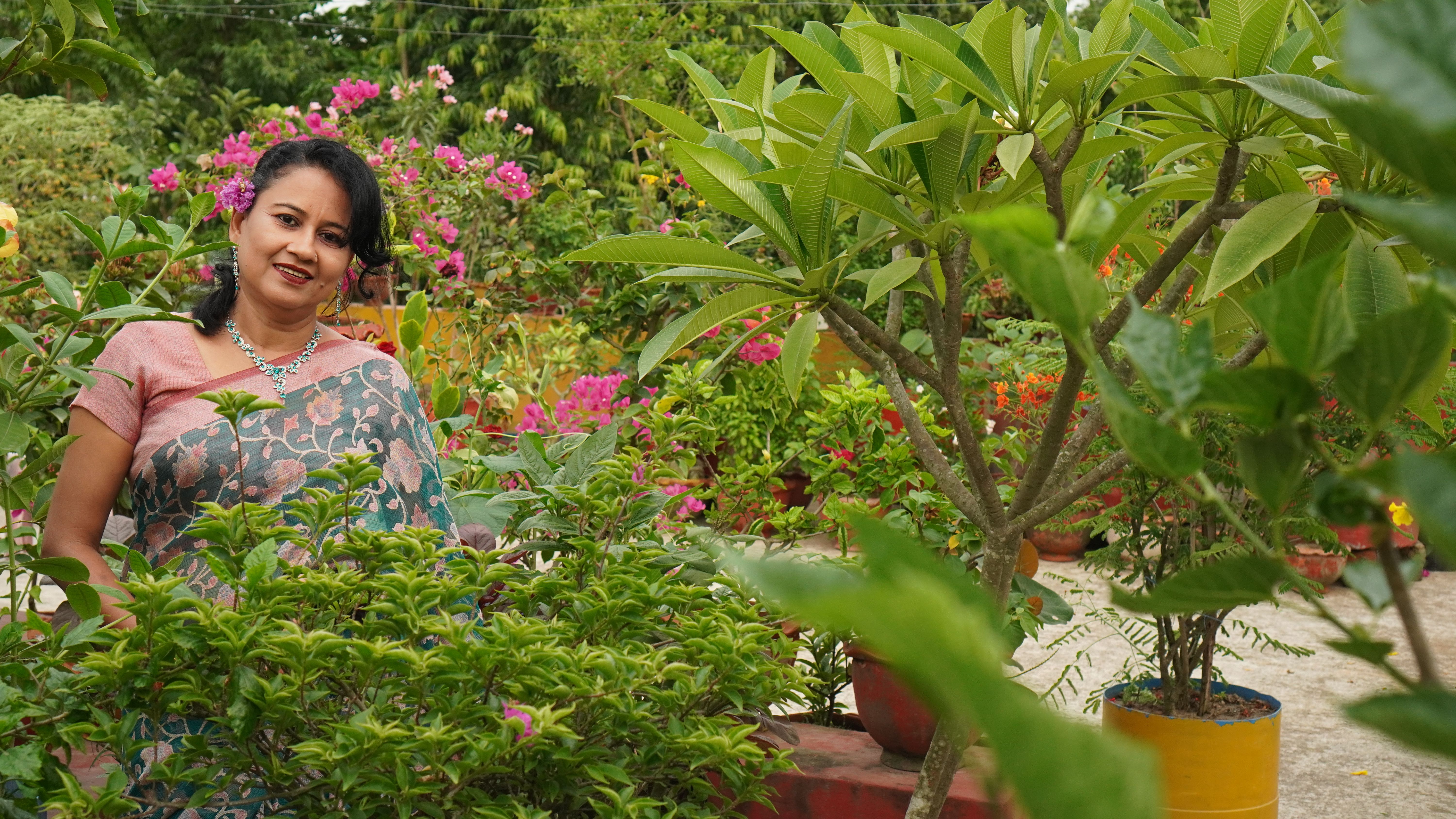 Smiling woman in a colorful garden surrounded by lush plants and flowers.