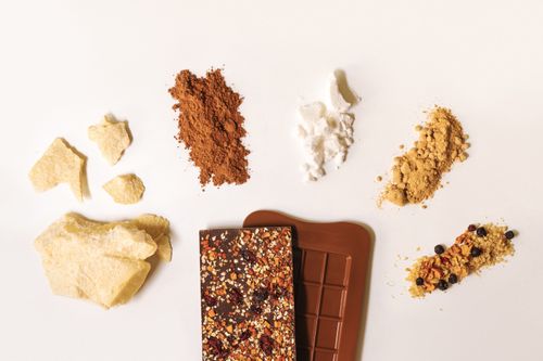 Free Flat lay of artisan chocolate bar surrounded by raw ingredients on a white background. Stock Photo