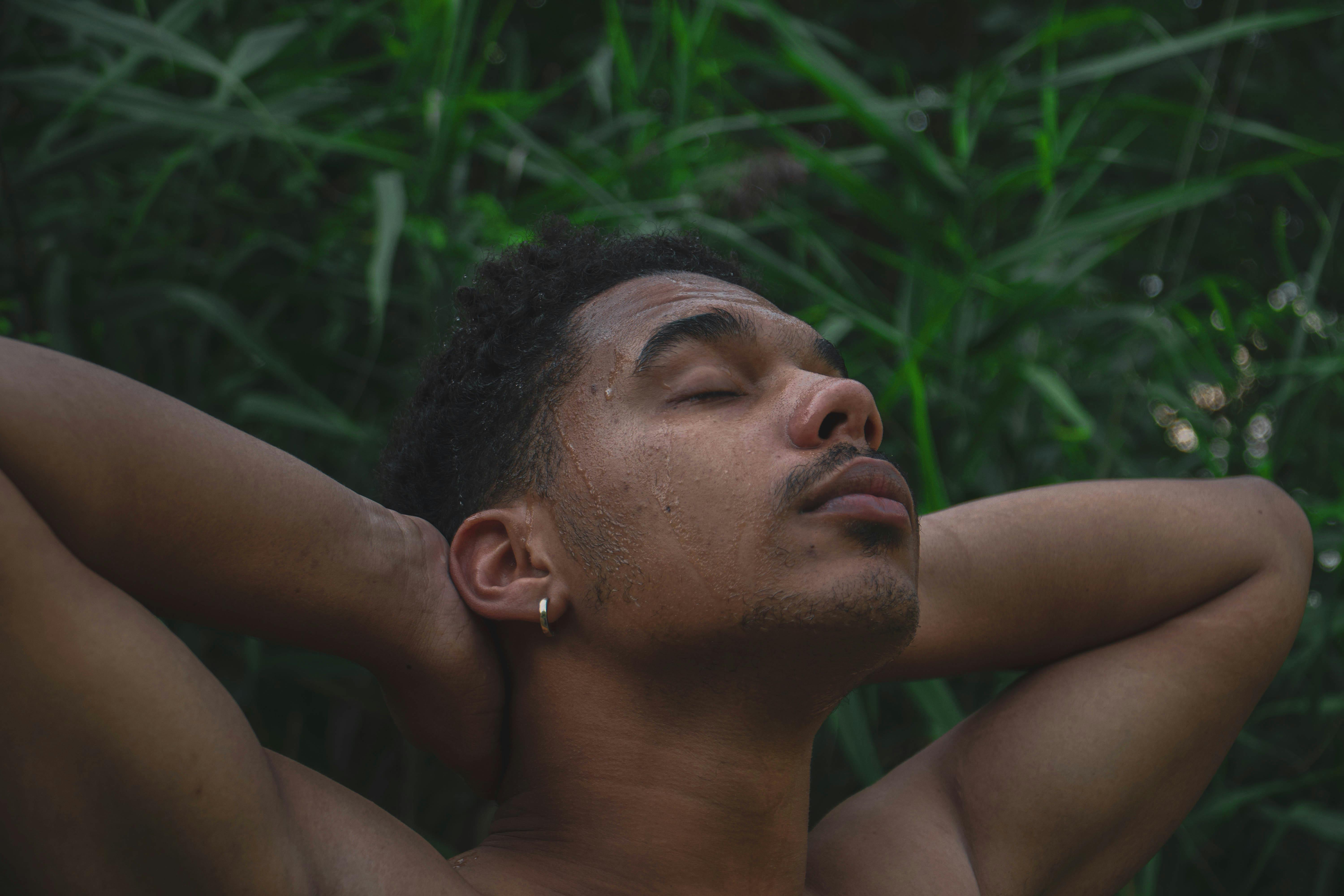 A shirtless man enjoying a calm moment outdoors with closed eyes.