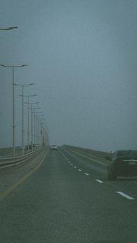 A moody, dimly lit highway with sparse evening traffic and street lamps lining the road.