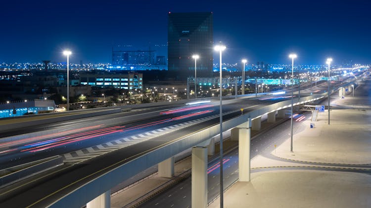 Photo Of An Empty Highway On A Viaduct Against The Background Of A Cityscape In The Night