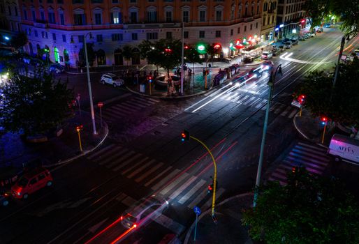 A dynamic aerial view of a city intersection at night, highlighted by vibrant light trails from moving cars.