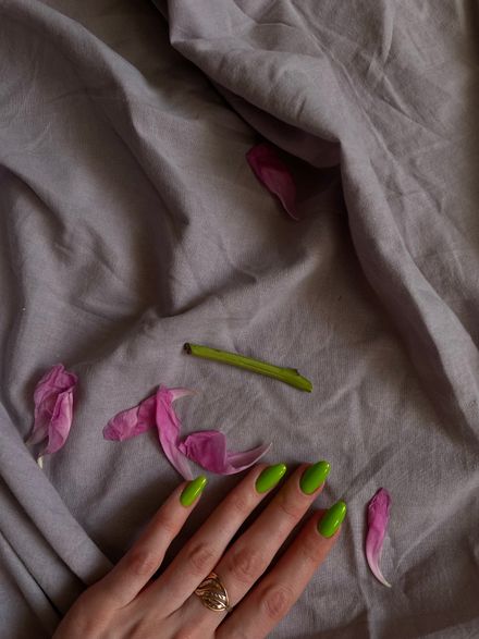 Lime-green nails and a gold ring on grey linen with magnolia petals — photo by Christina on Pexels