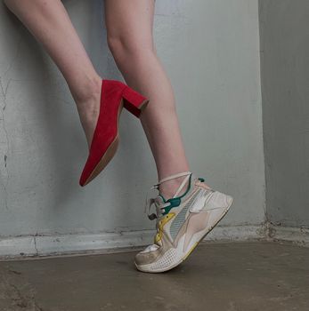 Creative shot of red high heel and sneaker on female legs, showcasing fashion contrast.