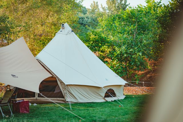 Canvas bell tent staked in a sunlit meadow beside trees — photo by SONIC on Pexels