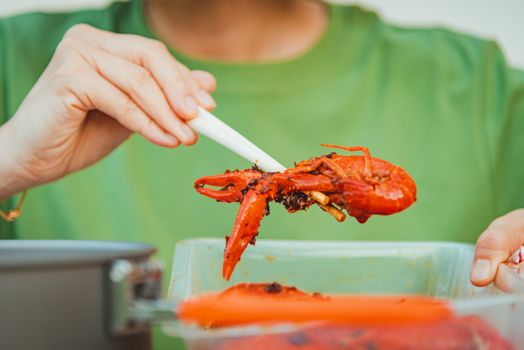 A hand using chopsticks to serve vibrant red lobster from a pot.
