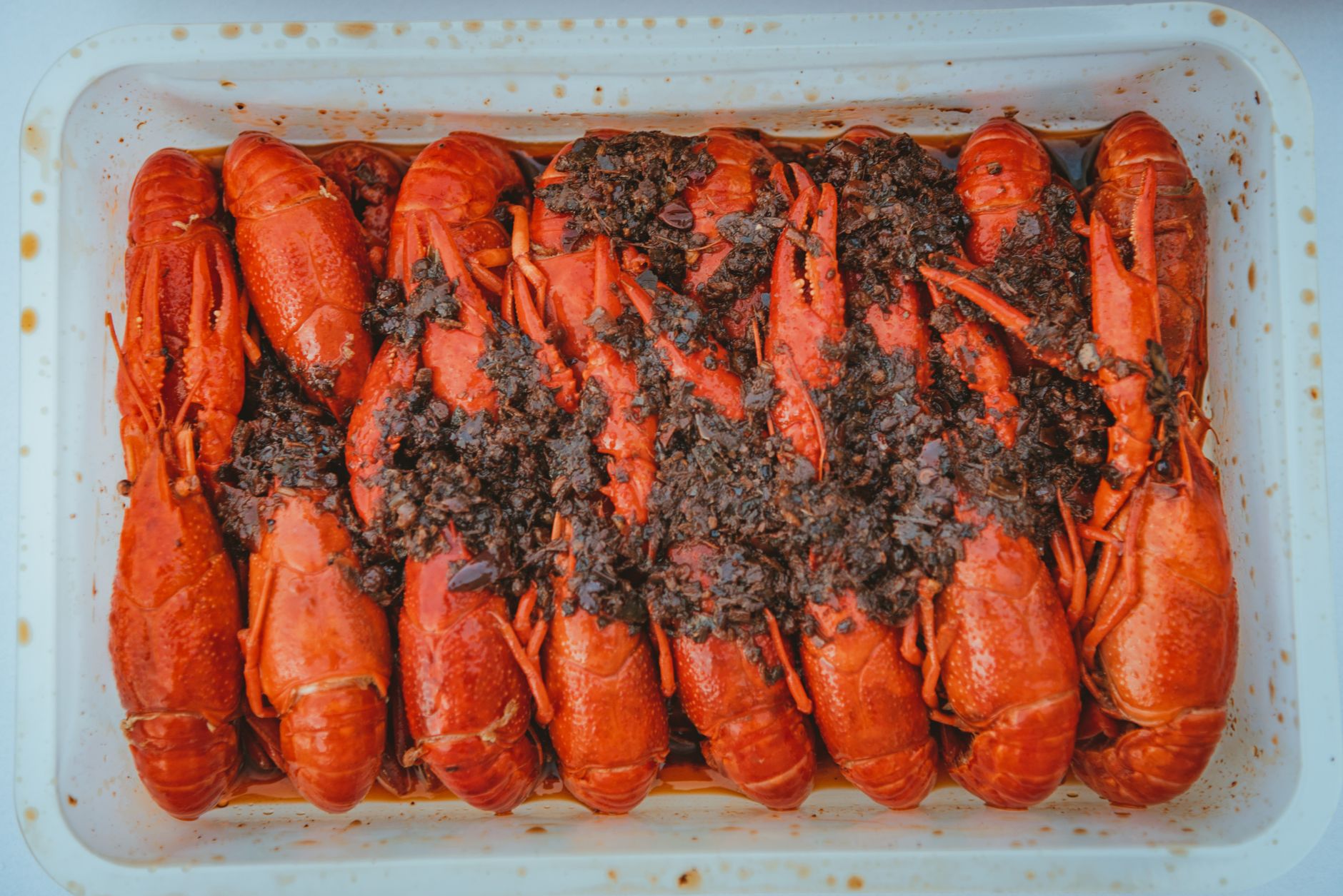 Mouthwatering cooked lobsters with seasoning in a white tray, perfect for seafood dining.