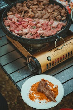 Juicy cuts of meat grilled on a portable stove, served Korean BBQ style on a picnic table.