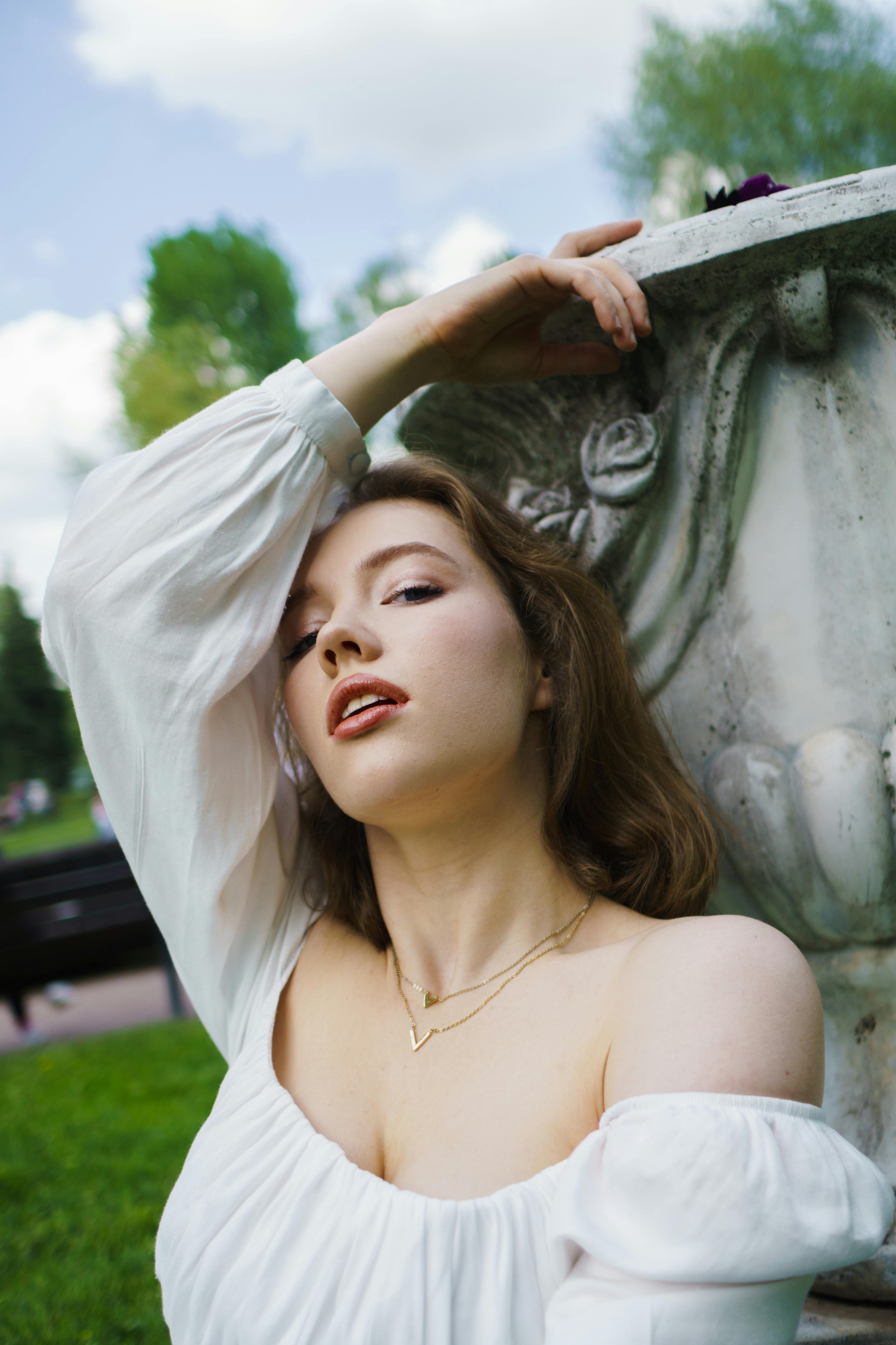 Elegant woman leaning against a sculpture, posing gracefully in a serene outdoor setting.