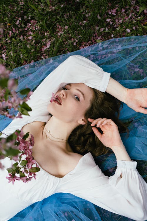 Woman in White Dress Lying on Blue Textile over the Grass