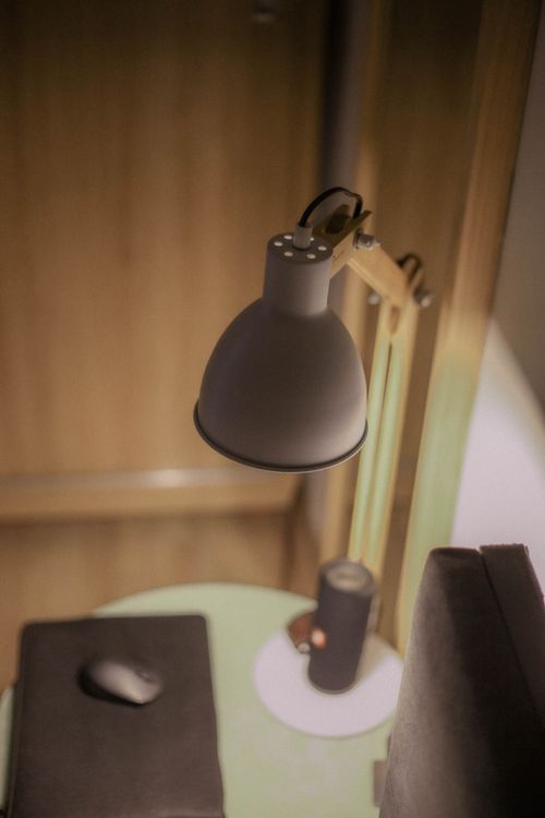 Free Close-up of a modern desk lamp in a cozy indoor setting, perfect for office or study environments. Stock Photo