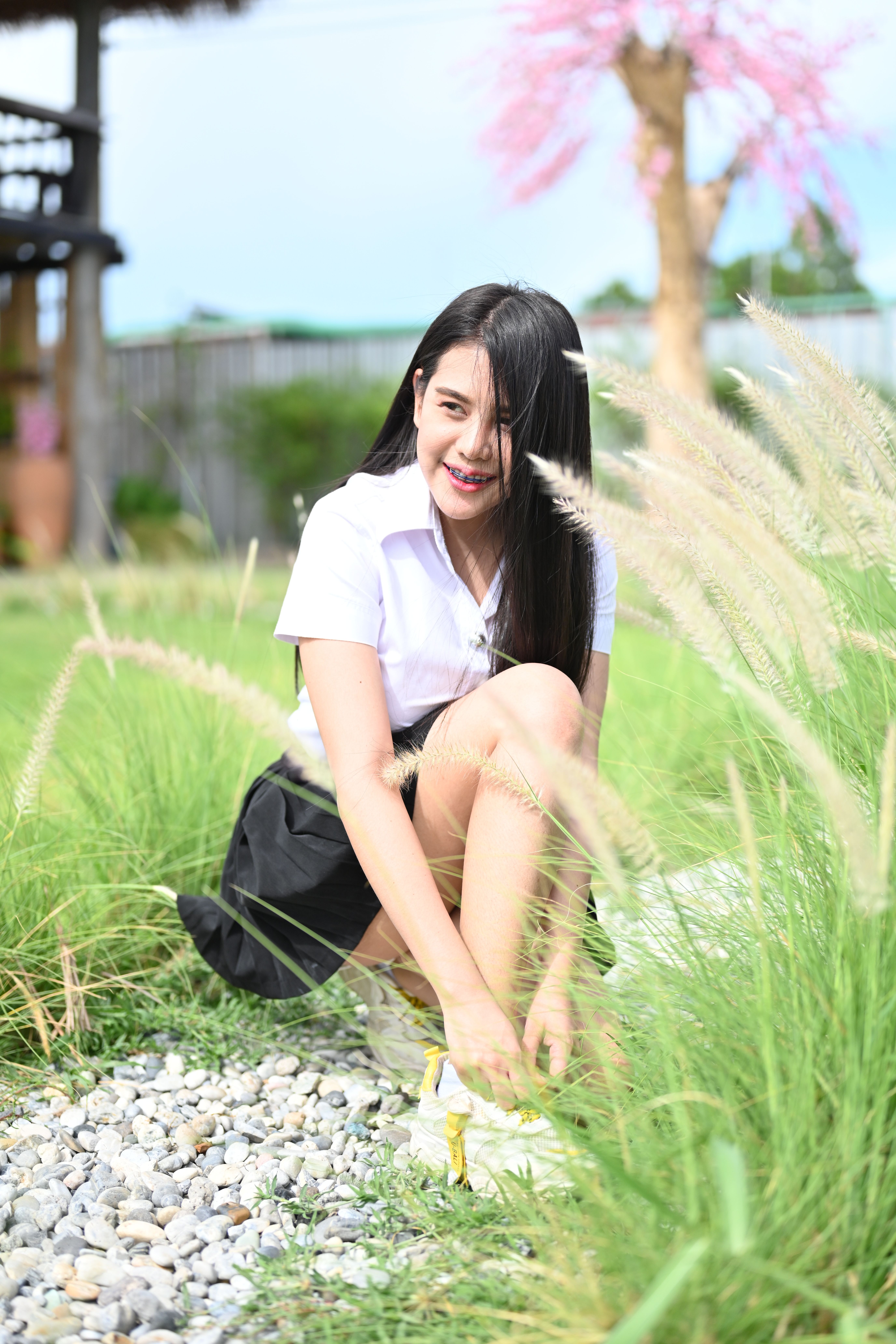 Asian woman kneeling in a vibrant outdoor garden tying her shoelaces on a sunny day.