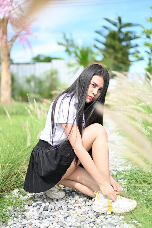 Free A young woman kneels outdoors, tying her shoes in a sunny garden setting. Stock Photo