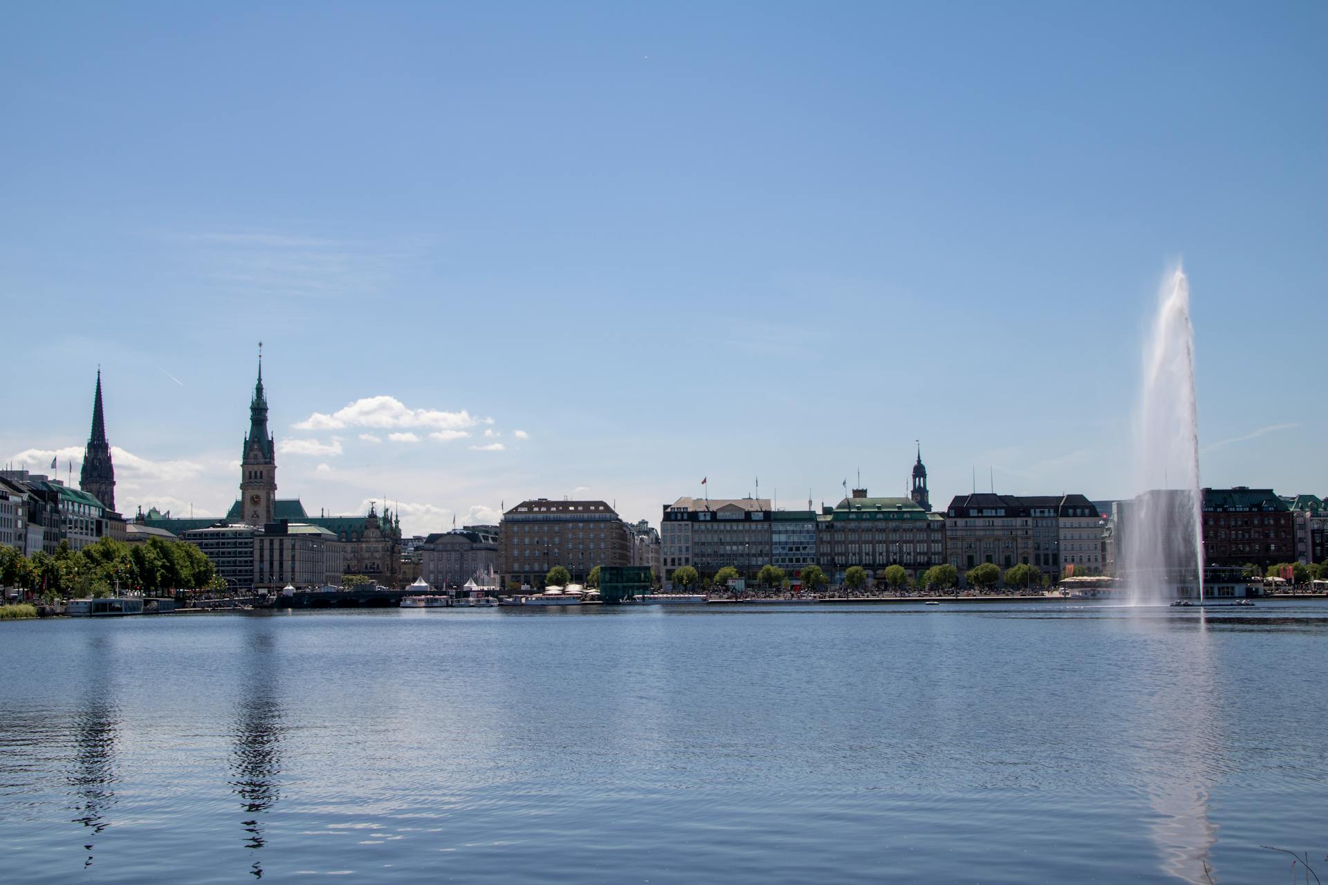 Beautiful Hamburg cityscape with Alster Lake and iconic fountain under a clear blue sky.