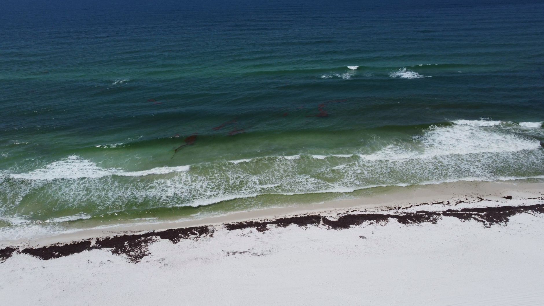 Aerial photograph showcasing the pristine blue waves and white sand of Pensacola Beach, Florida.