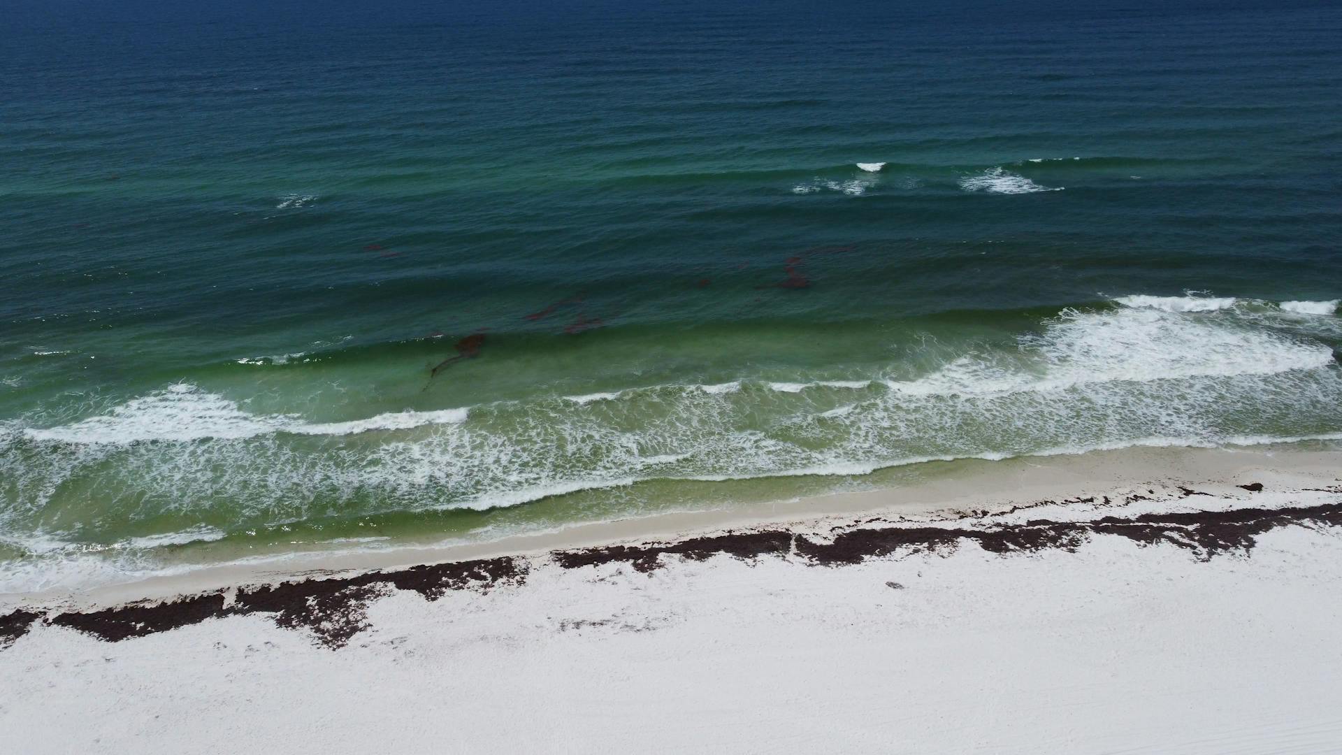 Aerial photograph showcasing the pristine blue waves and white sand of Pensacola Beach, Florida.