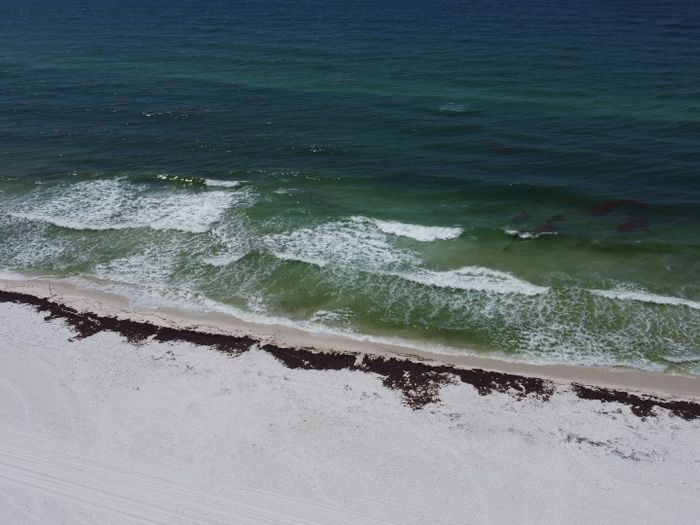 Aerial view of Pensacola Beach with waves crashing onto the shore under a summer sky.