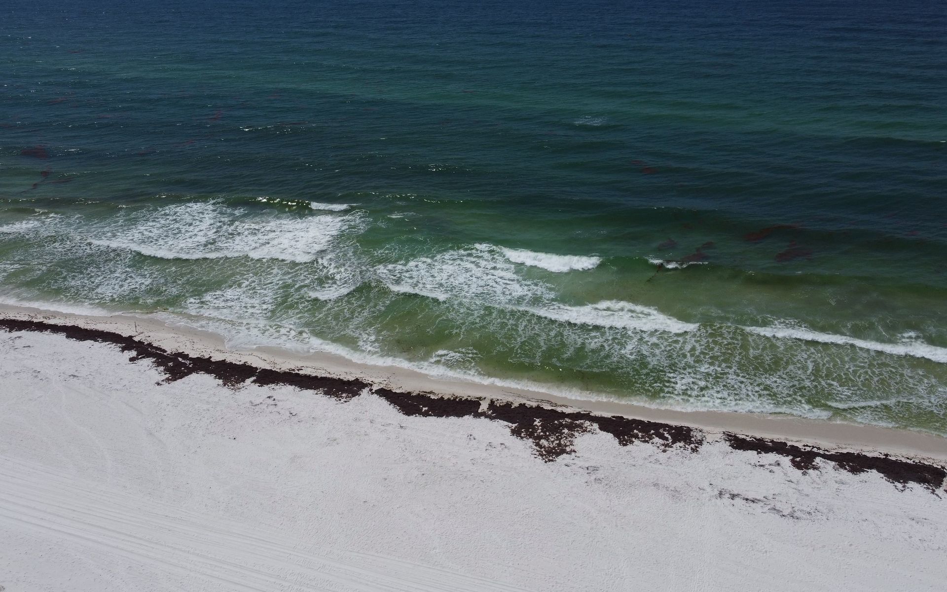 Aerial view of the pristine Pensacola Beach with waves crashing onto the shore under a summer sky.