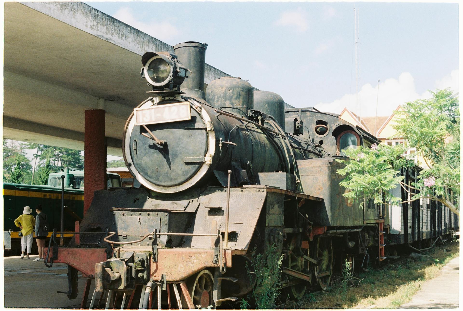 Old steam engine locomotive resting at a historical train station under the bright sky.