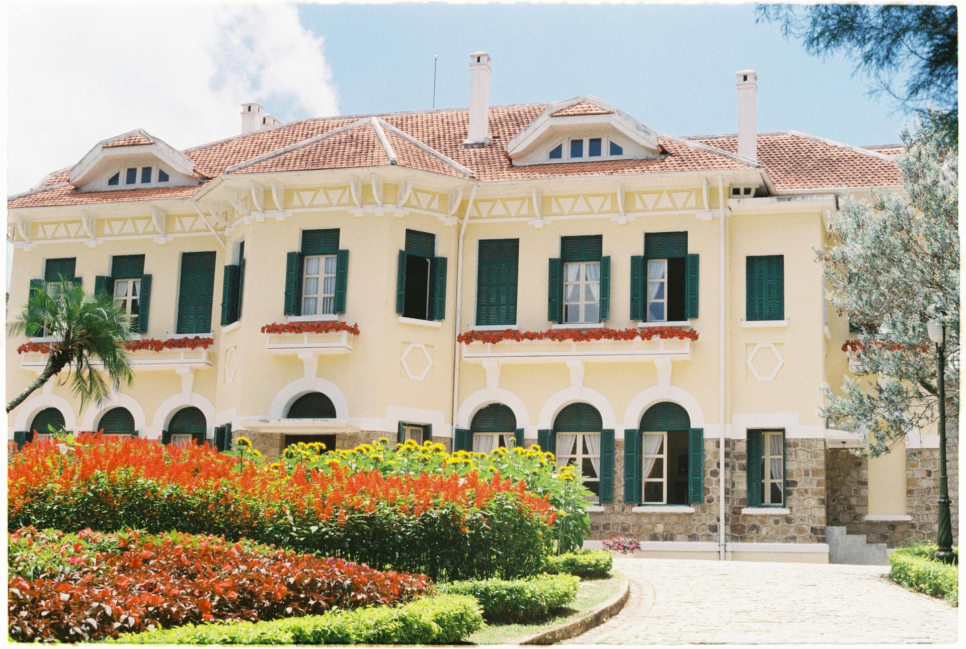 A picturesque historic house surrounded by vibrant flowers and manicured gardens.