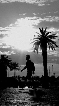 A striking silhouette of a man walking past palm trees during sunset, captured in monochrome.